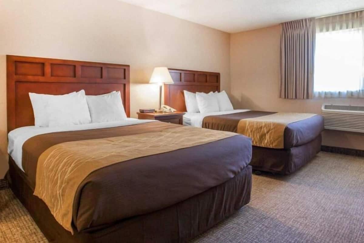 Quarto de hotel com duas camas, uma mesa de cabeceira, uma luminária e um ar condicionado.