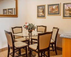 Un comedor con una mesa de vidrio rodeada de sillas a rayas, un florero con flores y cuadros en la pared.