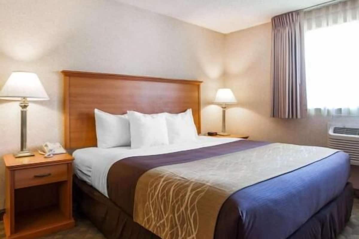 Quarto de hotel com cama, duas mesas de cabeceira com luminárias, janela com cortinas e ar condicionado fixado na parede.