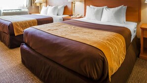 A hotel room with two beds, a nightstand, a lamp, and a telephone.