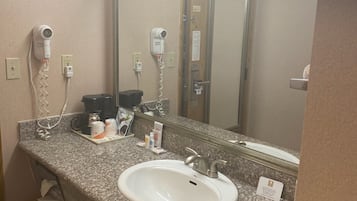 Un baño con encimera de granito, un lavabo blanco, un espejo, un secador de pelo y un refrigerador pequeño.