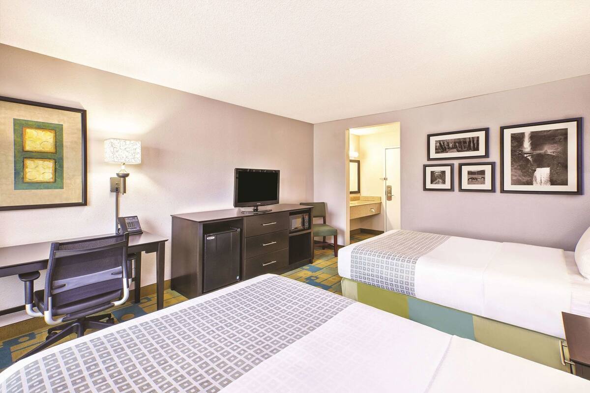 Habitación de hotel con dos camas, un escritorio con ordenador, televisor y un refrigerador pequeño.