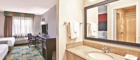A hotel room with a bed, desk, chair, and a bathroom with a sink and mirror.