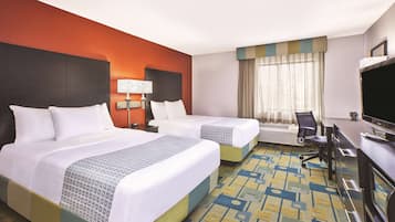 A hotel room with two beds, a desk, a chair, a TV, and a window with curtains.