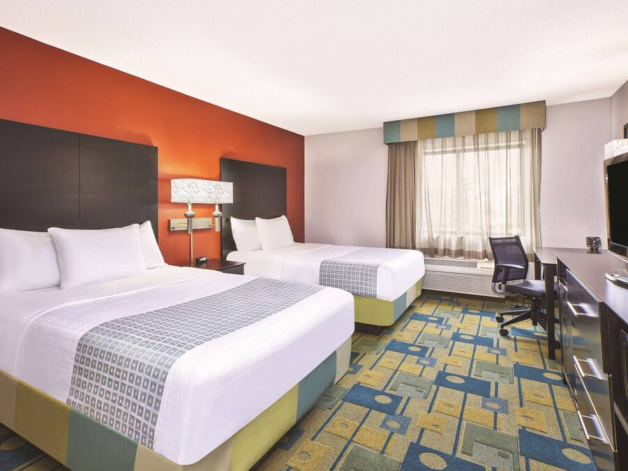 A hotel room with two beds, a desk, a chair, a TV, and a window with curtains.