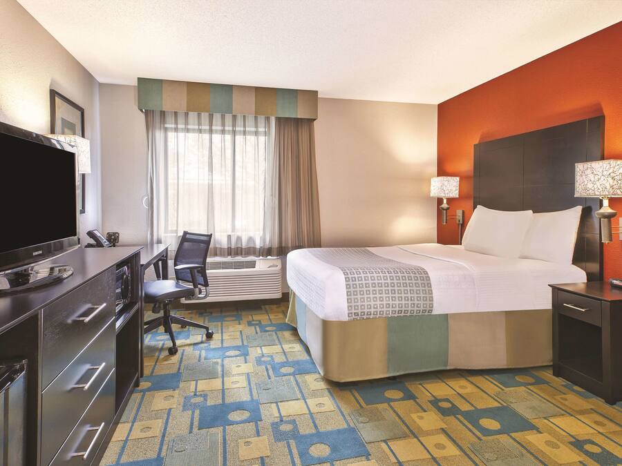 A hotel room with a bed, a desk with a TV, a chair, and a window with curtains.