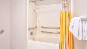 Un baño con bañera, barras de apoyo, cabezal de ducha y un perchero para toallas.