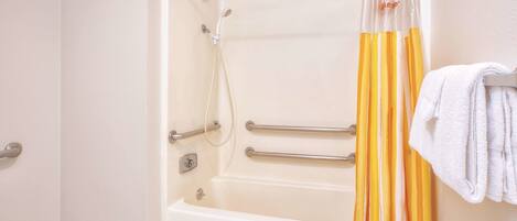 A bathroom with a bathtub, grab bars, a showerhead, and a towel rack.