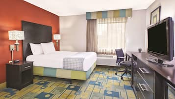 A hotel room with a bed, a desk with a computer, a TV, and a chair.