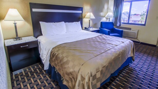 Une chambre d’hôtel avec un grand lit, deux tables de chevet avec des lampes, un fauteuil bleu et une fenêtre donnant sur un beau paysage.