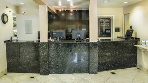 Un espace d’accueil doté d’un comptoir en marbre noir, de deux écrans d’ordinateur, d’une horloge et d’un panneau d’affichage contenant des informations sur l’hôtel.