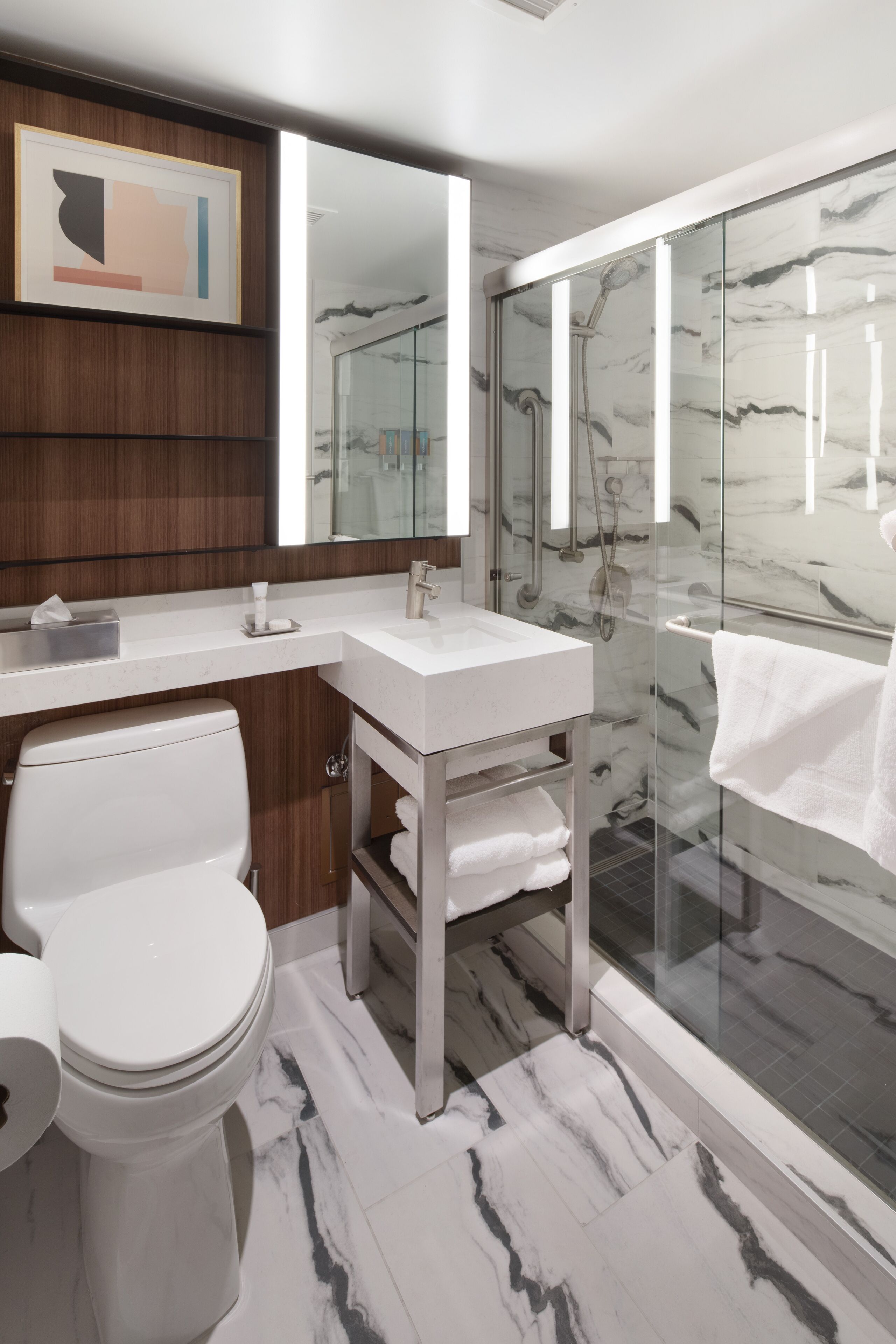 A modern bathroom with a marble floor, a white toilet, a vanity with a mirror, and a glass-enclosed shower area.
