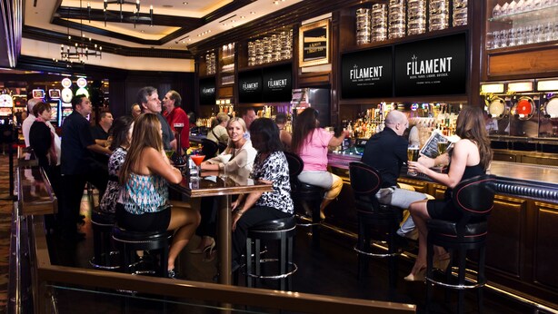 A bar area with multiple stools and tables, a well-stocked bar counter, and framed signs on the wall.