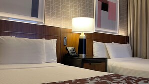 A hotel room with two beds, a bedside table with a lamp, a telephone, and artwork on the walls.