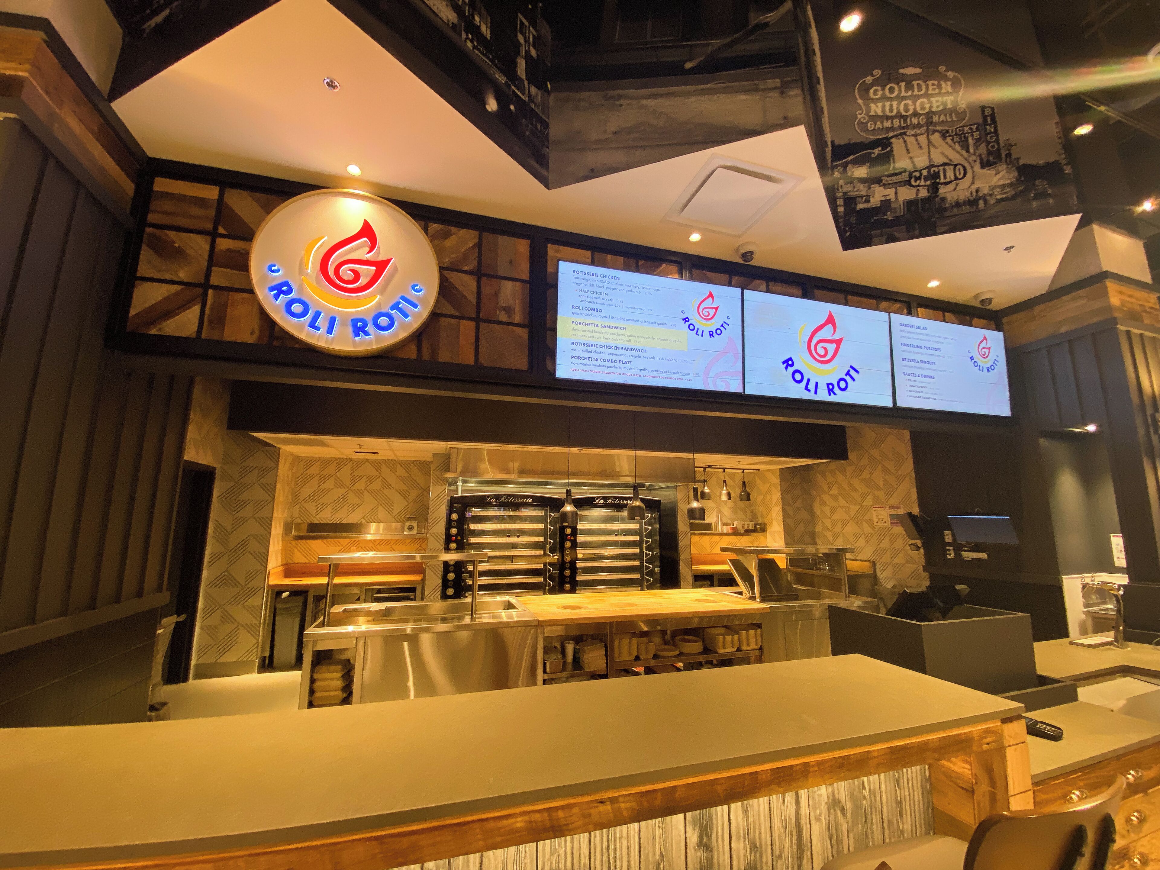 A restaurant interior with a modern design, featuring a central counter, a menu display, and a kitchen area with ovens.