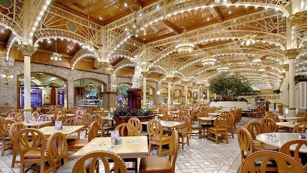 Un comedor amplio con mesas y sillas de madera, un diseño de techo ornamentado y una pieza decorativa central.