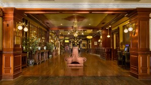 Un lobby de hotel imponente con un largo pasillo de madera, candelabros ornamentales y una chimenea decorativa en el centro.