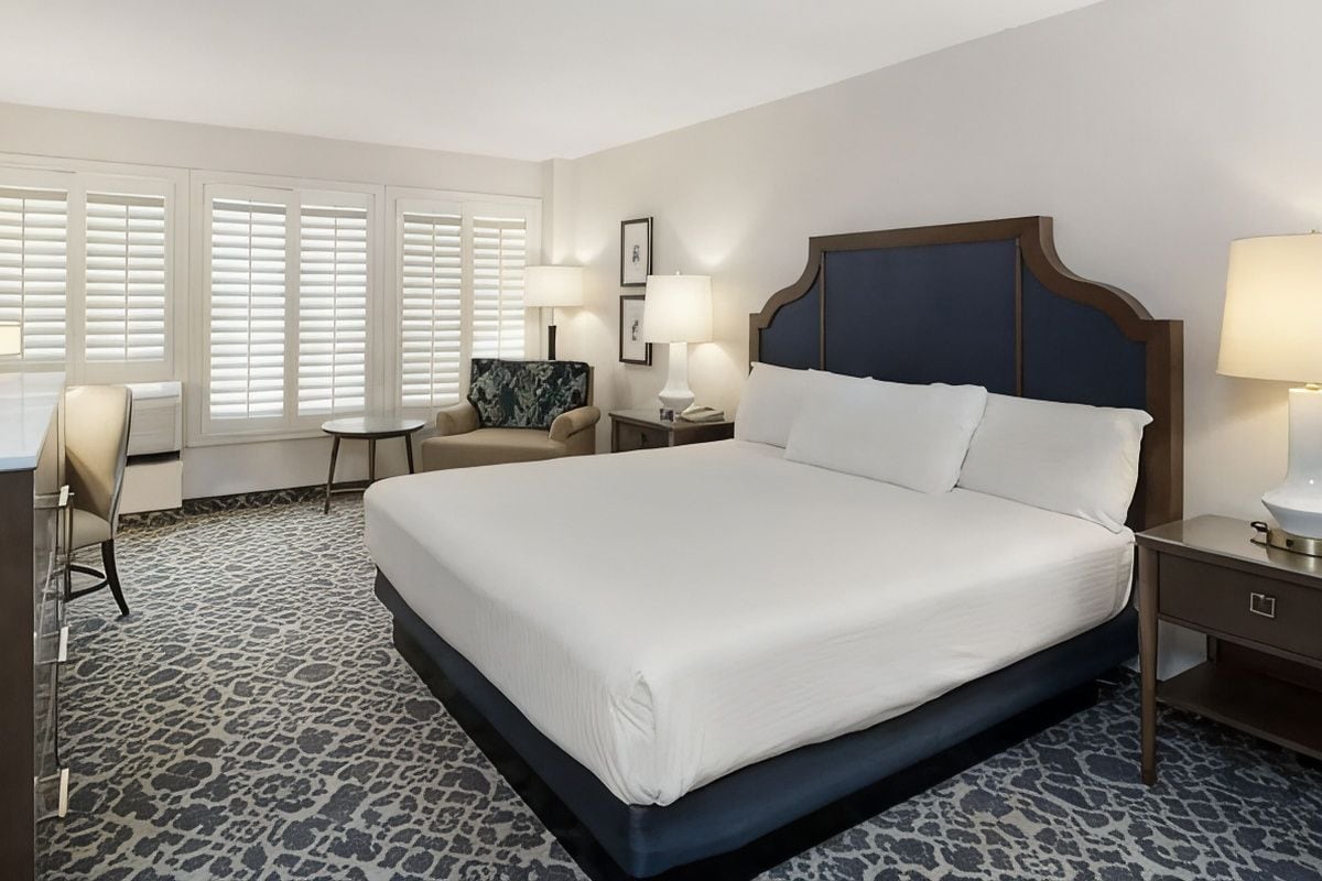 A hotel room with a large bed, a desk, a chair, and a small table.