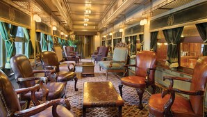 Interior de un vagón de tren antiguo con sillones de cuero, una mesa de madera y detalles ornamentales en el techo.