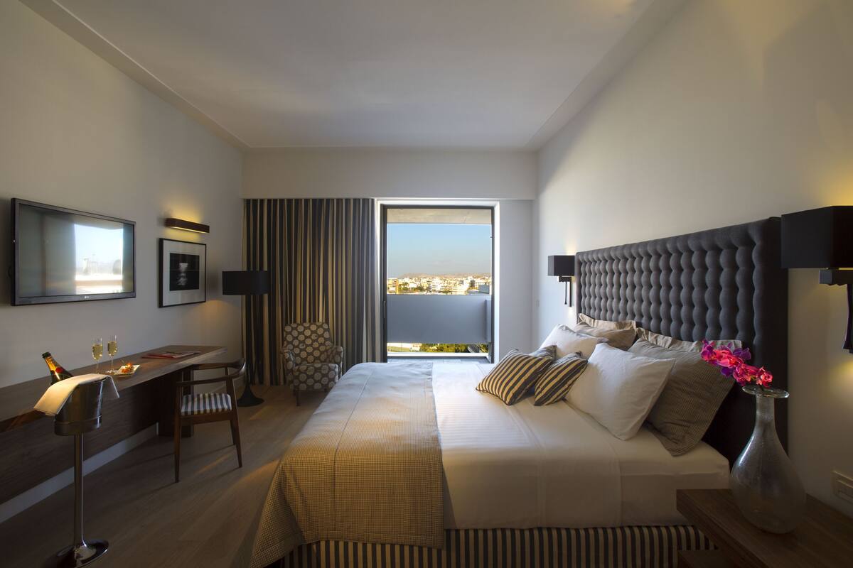 A modern hotel room with a large bed, a desk, and a view of the city.