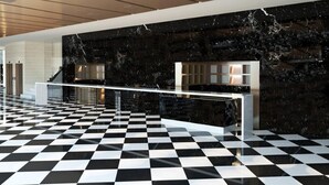 Um hall com piso quadriculado em preto e branco, parede de mármore e um balcão de recepção.