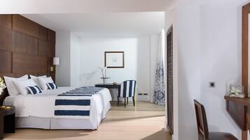 Une chambre d’hôtel moderne avec un grand lit, un bureau et une chaise. On y trouve une fenêtre avec des rideaux, un tableau encadré au mur et une petite table avec une lampe.