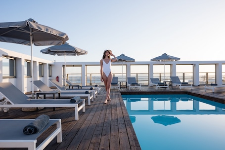 A poolside area with lounge chairs and umbrellas, a wooden deck, and a clear view of the sea.