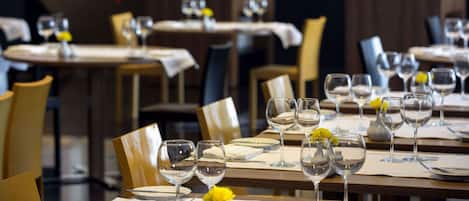 Un restaurante con mesas dispuestas para comer, con manteles blancos, copas de vino y pequeños jarrones con flores amarillas.