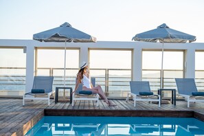 A poolside area with lounge chairs and umbrellas, overlooking a body of water. - Aquila Atlantis Hotel (Heraklion)
