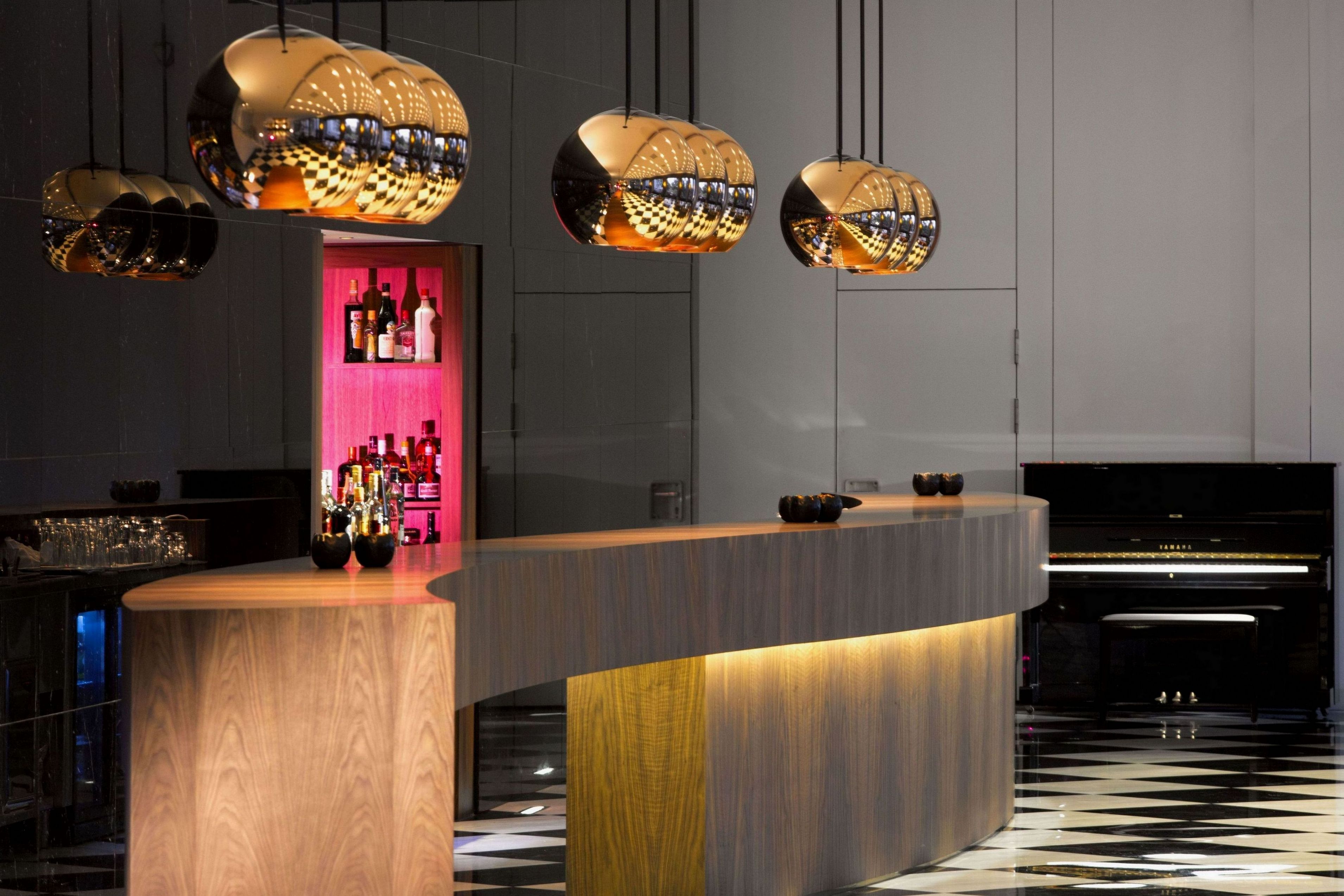 A modern bar area with a curved wooden counter, hanging spherical light fixtures, and a checkered floor.