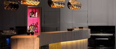 A modern bar area with a curved wooden counter, hanging spherical light fixtures, and a checkered floor.