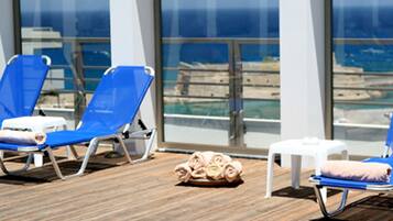 A poolside area with lounge chairs, a small table, and a view of the ocean.