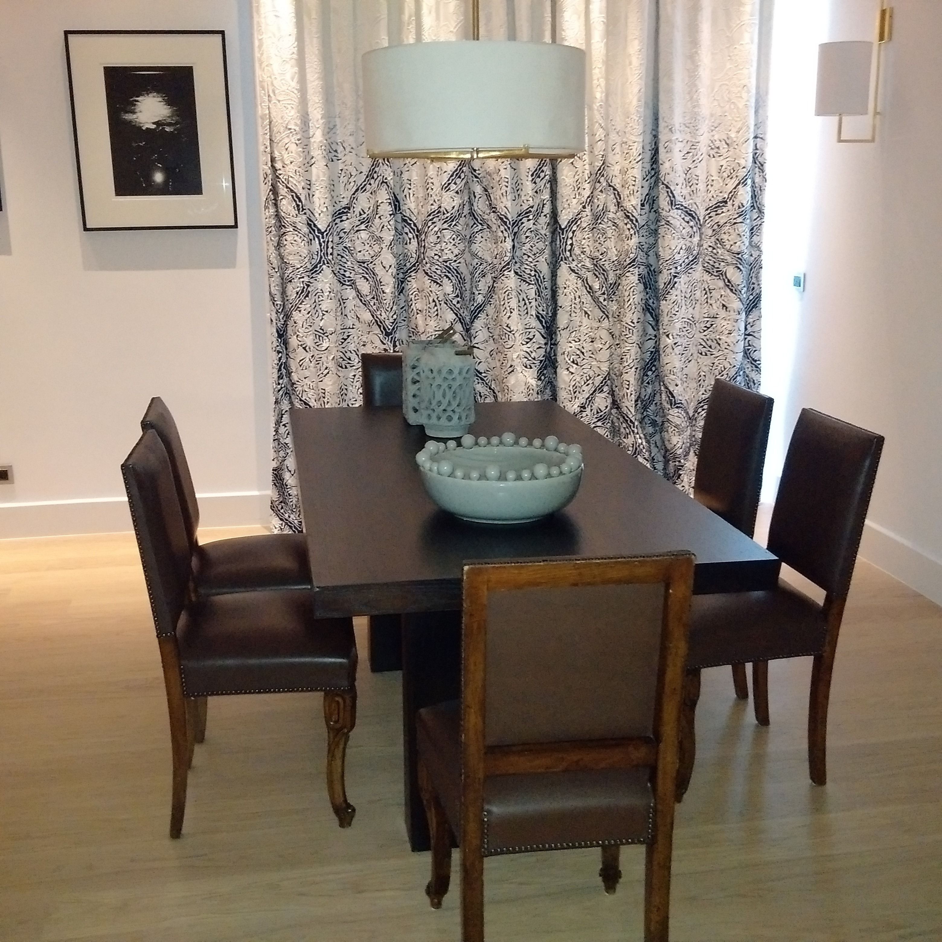 A dining area with a dark wooden table, four upholstered chairs, a white bowl, and a table lamp.