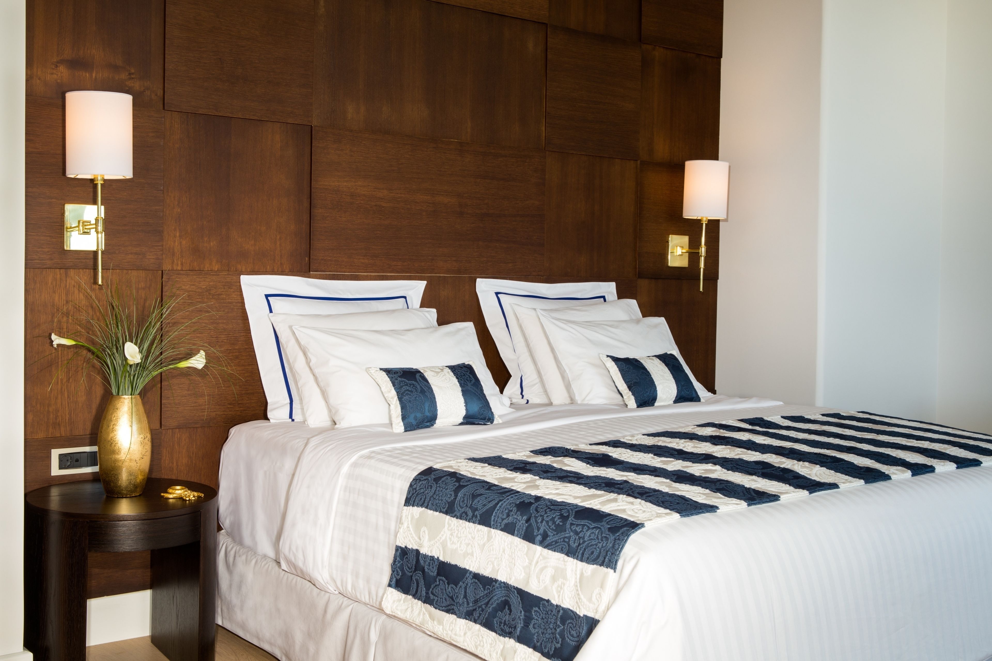 A neatly made bed with a striped bedspread, two bedside lamps, and a vase with flowers on a nightstand.
