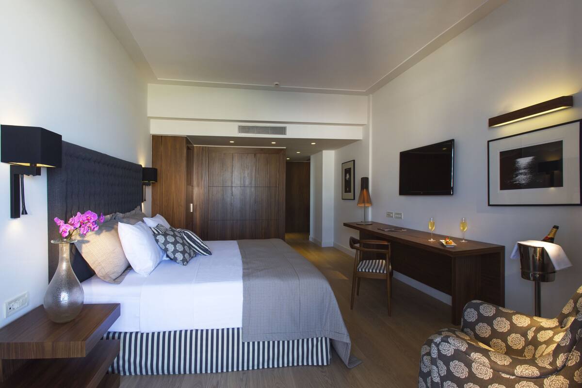 A modern hotel room with a bed, bedside table, desk, chair, and a TV on the wall.