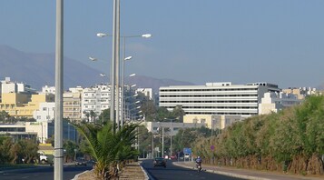 Uma rua urbana com edifícios, postes de luz e veículos.