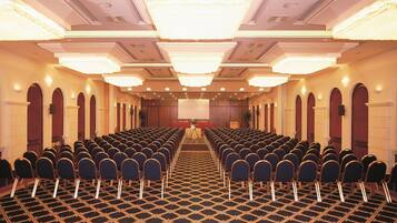 A conference room with rows of chairs, a stage, and chandeliers.
