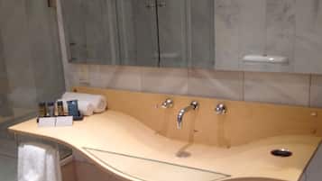 Un baño con un lavamanos curvo, una cabina de ducha con mampara de vidrio y un revestimiento de mármol en la pared.