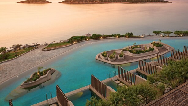 Een resort zwembad met verschillende zones, omringd door aangelegde groene ruimtes en verre eilanden.