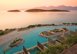 Een resort zwembad met verschillende zones, omringd door aangelegde groene ruimtes en verre eilanden.