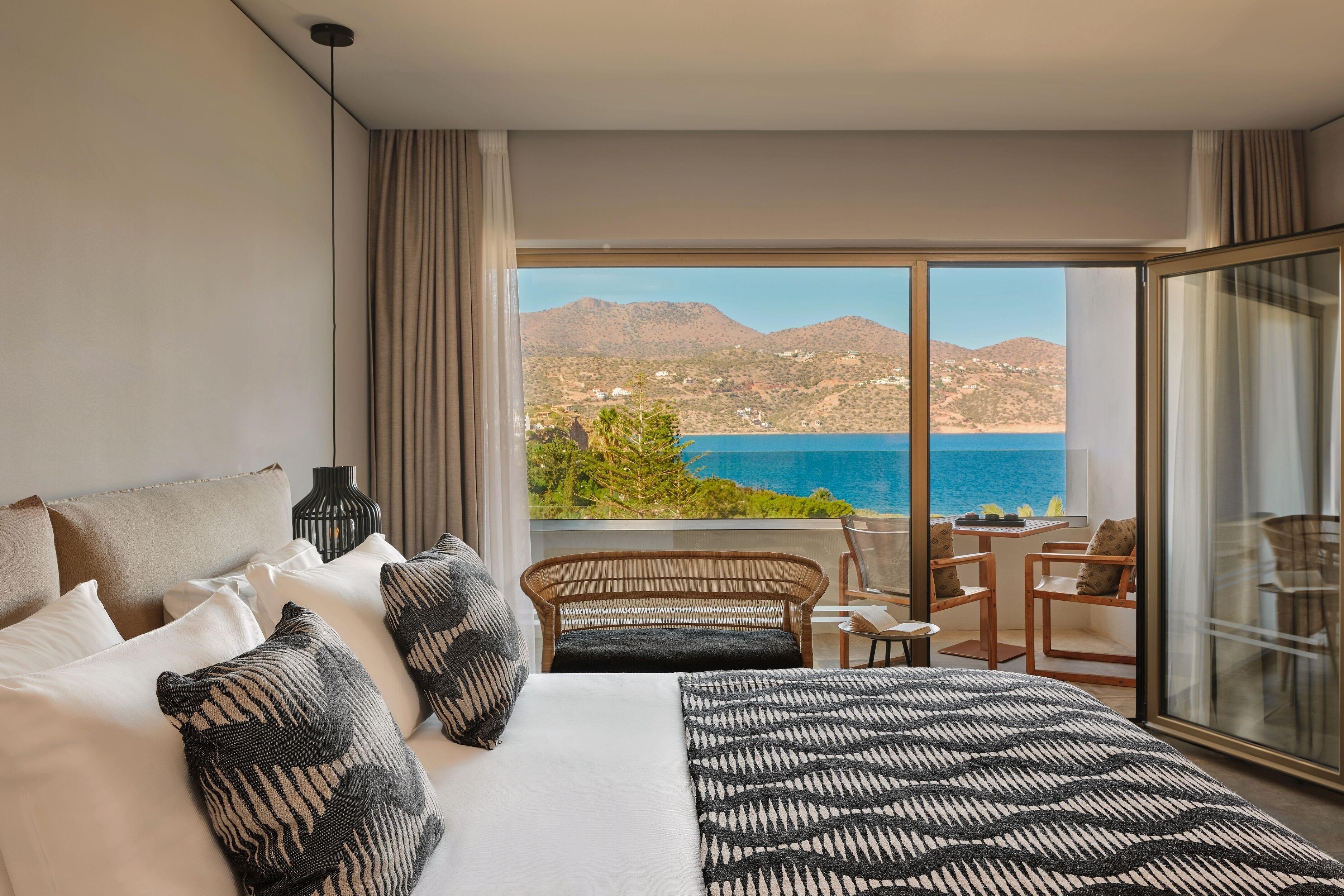 Quarto com cama grande, vista para o mar e varanda com assentos.