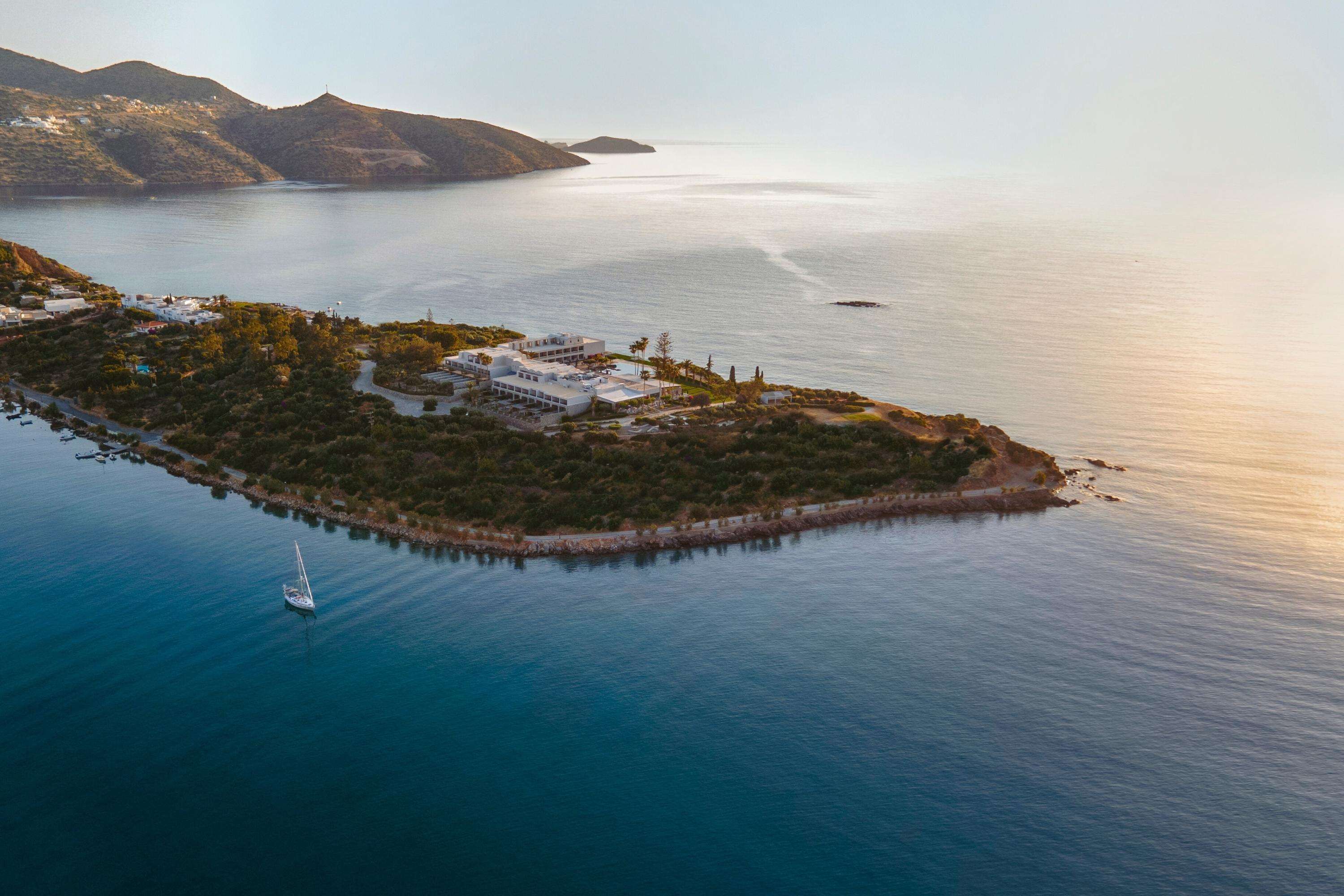 Vista aérea de una isla costera con un puerto deportivo, edificios y una vista despejada del mar y las montañas circundantes.