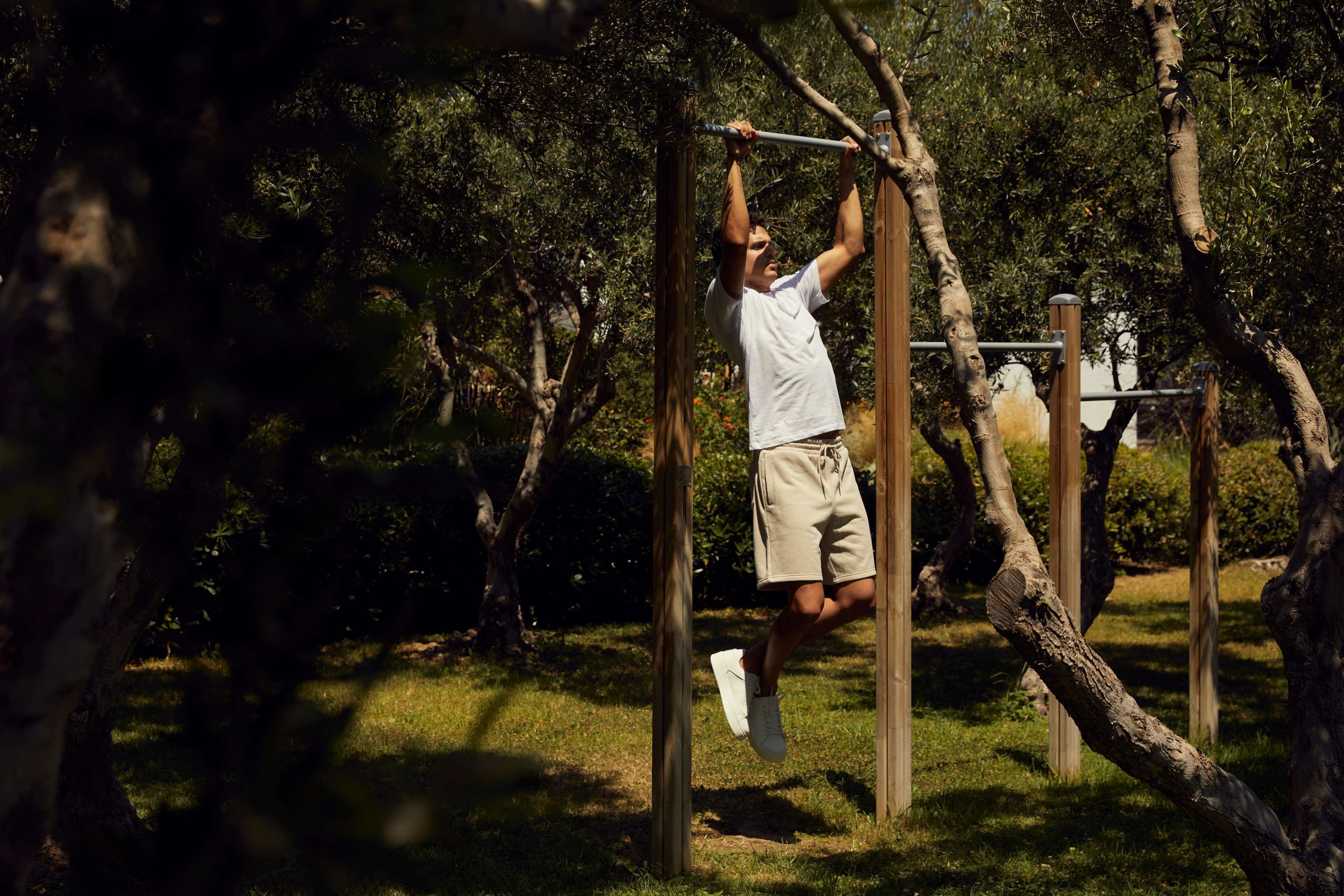 A person hanging from a horizontal bar in an outdoor setting with trees and grass.
