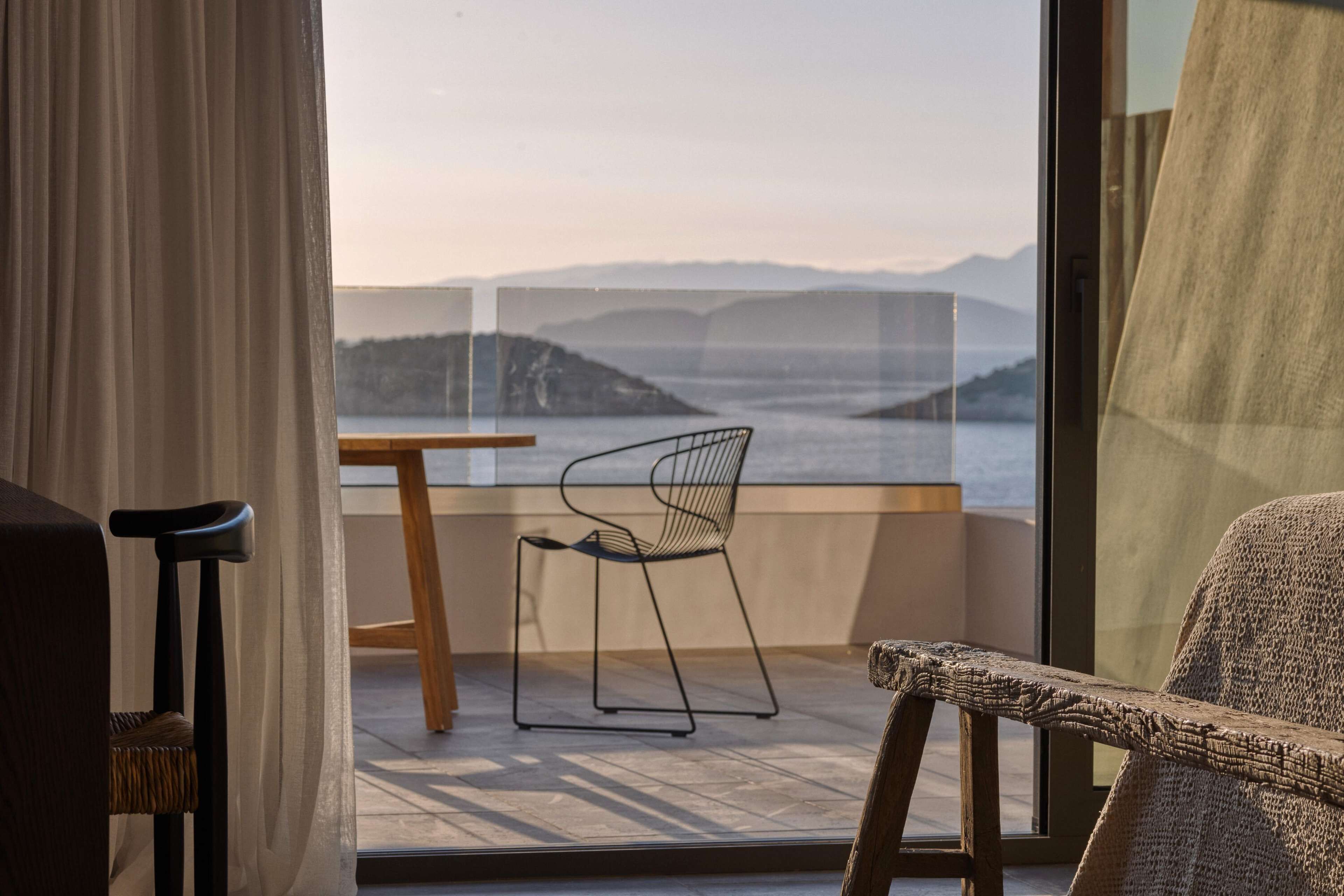A balcony with a view of the sea and mountains, a table, and two chairs.
