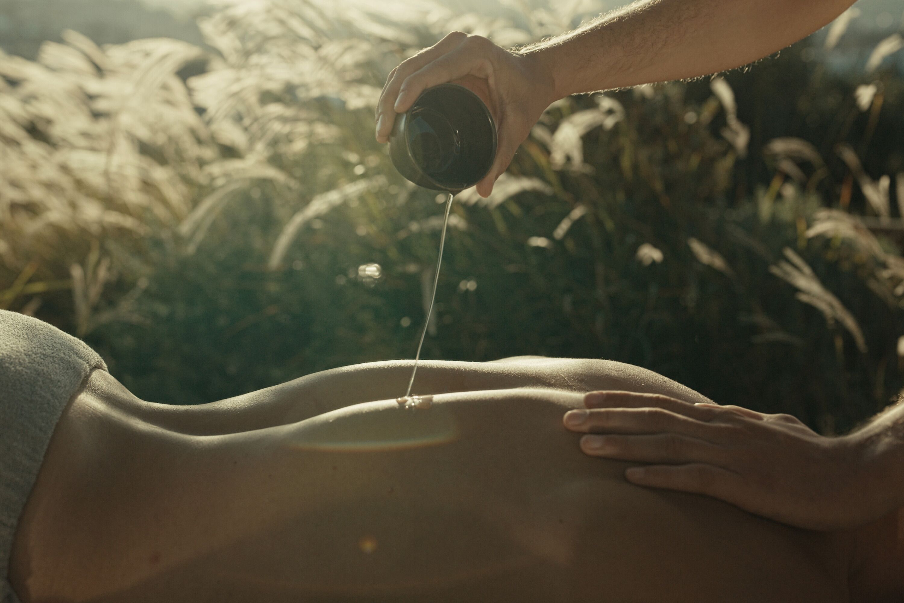 Uma pessoa recebendo massagem, com uma mão aplicando pressão e outra derramando um líquido nas costas.