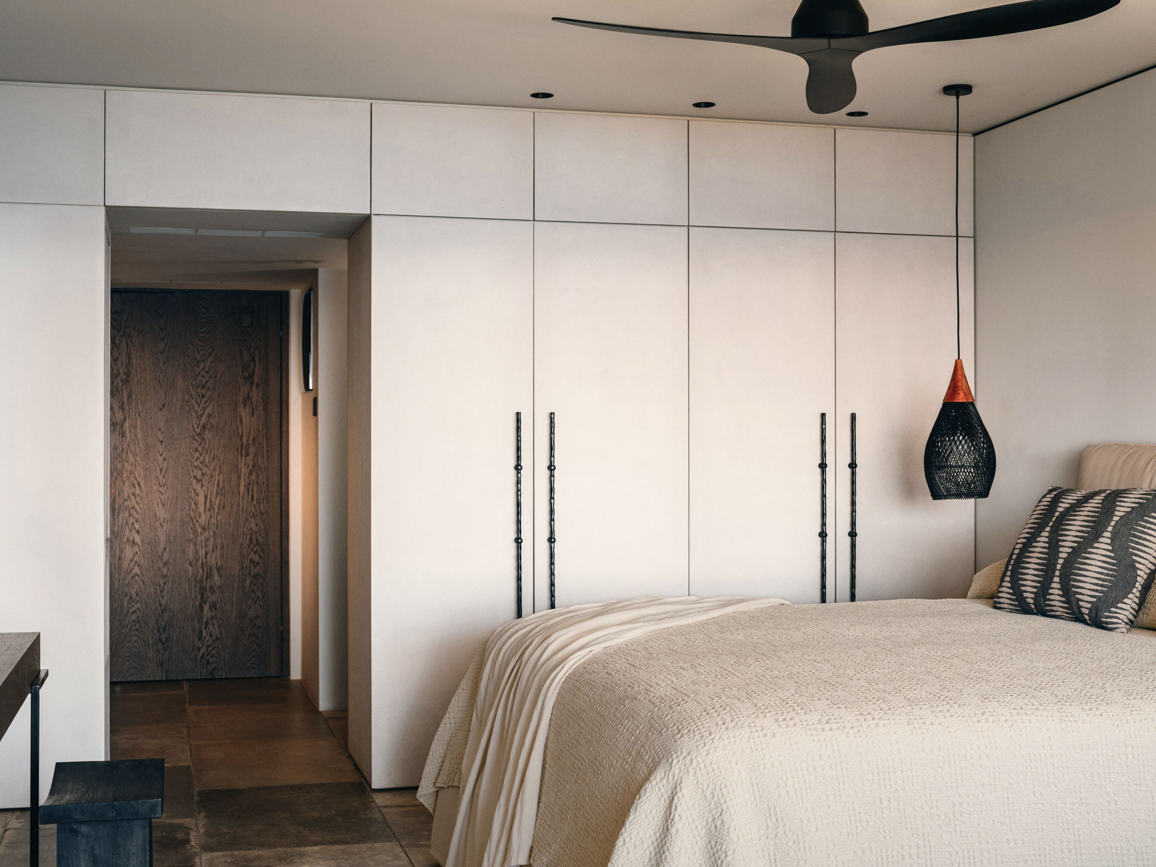 Un dormitorio moderno con una cama grande, un ventilador de techo y un armario con puerta de madera.