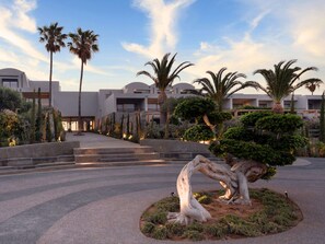 A modern hotel with a central courtyard featuring a large tree sculpture, palm trees, and a well-maintained garden. - Minos Palace Resort - Adults Only (Agios Nikolaos)