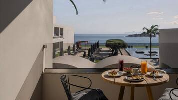 A balcony with a table set for breakfast, overlooking a pool and a view of the sea.
