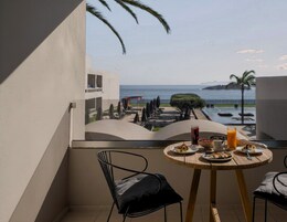 Un balcón con una mesa dispuesta para el desayuno, con vista a una piscina y al mar.