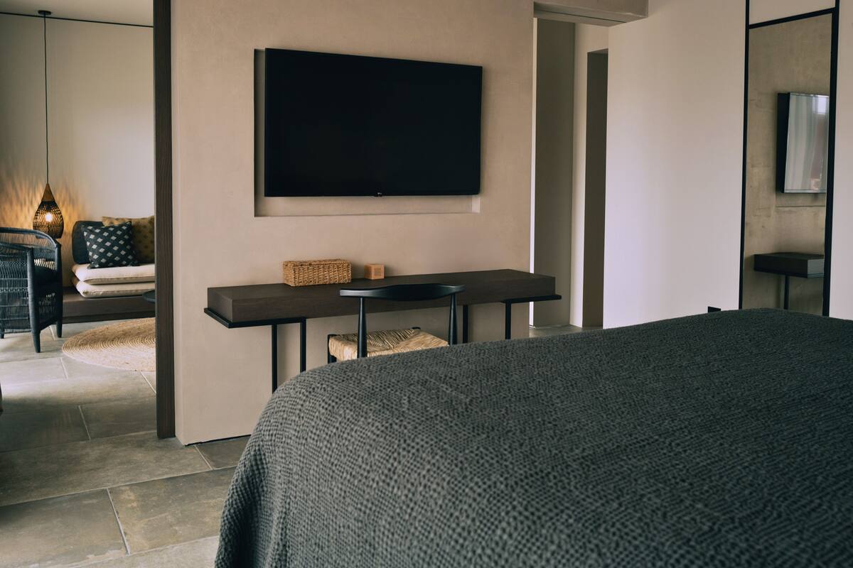 Een moderne hotelkamer met een groot bed, een flatscreen televisie aan de muur, een tafeltje met een mand en een zithoek met een bank en een stoel.